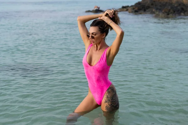 时尚浪漫柔嫩 体形健美 身材苗条 穿着粉色泳衣的性感女子 日落时在海滩上戴太阳镜 — 图库照片