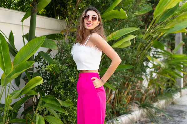 スタイリッシュなフィット日焼けした美しい女性でサングラス ファッションピンクのパンツとホワイトトップポージング屋外で高級トロピカルヴィラ — ストック写真