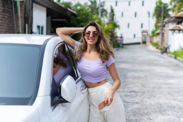 穿着休闲装 面带笑容的漂亮女人的成功秘诀是 站在豪华的现代汽车旁 用她的智能手机 — 图库照片