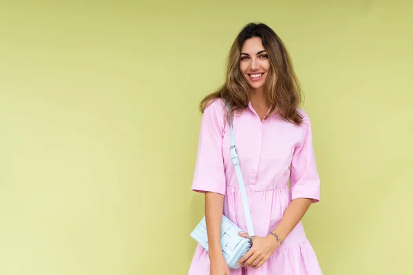 カジュアルなピンクの夏の綿のドレスの若い女性は緑の背景に隔離された着用かわいい青ショルダーバッグ幸せな大きな笑顔を保持 — ストック写真