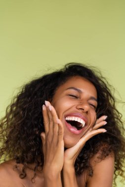 Yeşil arka planda çıplak omuzlu, mükemmel ciltli ve doğal makyajlı genç üstsüz Afrikalı Amerikalı kadının güzel portresi.