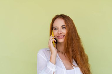 Yeşil arka planda rahat gömlekli güzel kızıl saçlı kadın. Cep telefonu tebessümü ve kahkahalar.