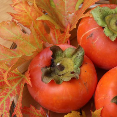 Tahta bir masada sonbahar yapraklı cam bir kasede olgun kaki ya da Persimmon meyveleri. Diospyros kaki meyveleri