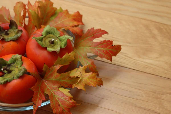 成熟的Kaki或Persimmon水果在一个玻璃碗与秋天的叶子木桌上 红辣椒的果实 — 图库照片