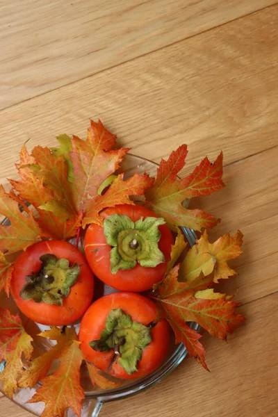 成熟的Kaki或Persimmon水果在一个玻璃碗与秋天的叶子木桌上 红辣椒的果实 — 图库照片