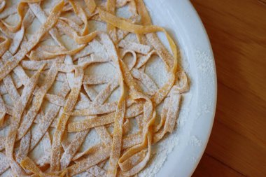 Ev yapımı İtalyan geleneksel balkabağı Tagliatelle makarnası ve ahşap masa üzerinde un. Çiğ İtalyan makarnası da fettucine, tagliatelle veya pappardelle olarak da bilinir.