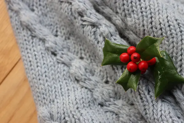 コピースペースとニット編組ウールパターンに多くの赤いベリーを持つ小さなホリーの枝 クリスマスのお祝いの背景 — ストック写真