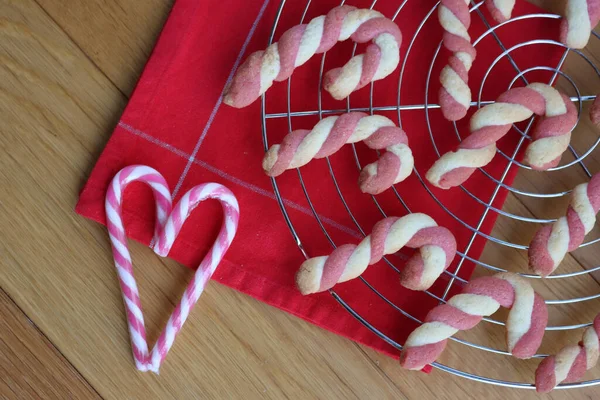 Christmas cookies in shape of a candy cane on a wire rack with red tablecloth with real candy canes in shape of heart