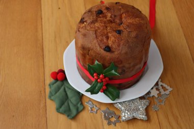 Geleneksel İtalyan Noel pastası Panettone kırmızı kurdeleli ve Holly dalı ahşap masa üzerinde kırmızı böğürtlenli.