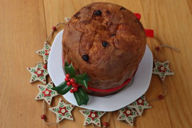 Geleneksel İtalyan Noel pastası Panettone kırmızı kurdeleli ve Holly dalı ahşap masa üzerinde kırmızı böğürtlenli.