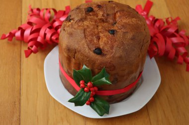 Geleneksel İtalyan Noel pastası Panettone kırmızı kurdeleli ve Holly dalı ahşap masa üzerinde kırmızı böğürtlenli.