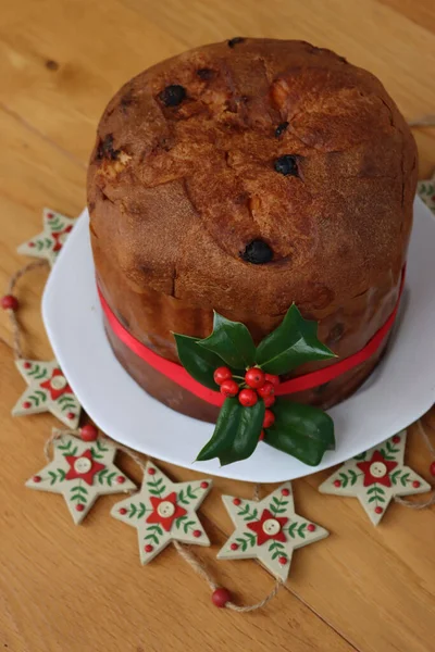 伝統的なイタリアのクリスマスケーキは 木製のテーブルの上に赤いリボンと赤い果実とホリーの枝とPanettoneと呼ばれます — ストック写真