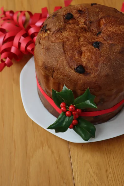 伝統的なイタリアのクリスマスケーキは 木製のテーブルの上に赤いリボンと赤い果実とホリーの枝とPanettoneと呼ばれます — ストック写真