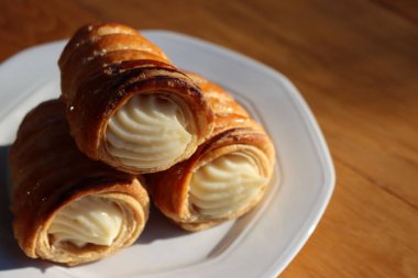 İtalyan geleneksel Cannoli. Tahta masadaki vanilyalı krema ile dolu.