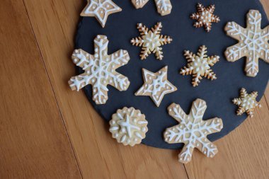 Yıldızlar ve kar taneleri şeklinde bayramlık zencefilli kurabiyeler. Tahta masadaki siyah taş tabakta.