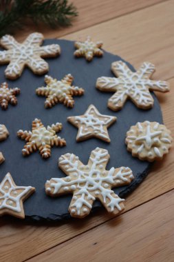 Yıldızlar ve kar taneleri şeklinde bayramlık zencefilli kurabiyeler. Tahta masadaki siyah taş tabakta.