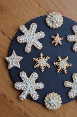 Yıldızlar ve kar taneleri şeklinde bayramlık zencefilli kurabiyeler. Tahta masadaki siyah taş tabakta.
