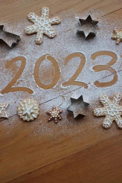 Tahta masaya serpiştirilmiş un üzerine zencefilli kurabiyeler serpiştirilmiş 2023 numaranın en üst görüntüsü. Mutlu Noeller ve mutlu yıllar 2023