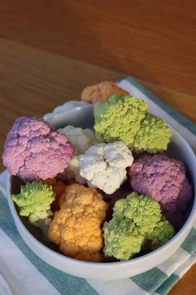 Various sort of cauliflower in a bowl on wooden table. Purple, yellow, white and green color cabbages and  green Romanesco or Roman cabbage