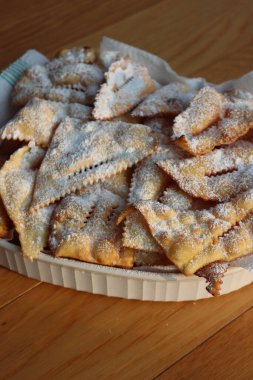 İtalyan Karnaval pastası. Geleneksel karnaval tatlı kıtır börek kızartılmış ve üzerine pudra şekeri serpiştirilmiş. Chiacchere veya crostoli, bugie, sanci beyaz bir tabakta ahşap masada 