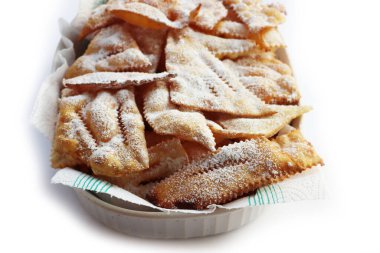 Traditional sweet crisp pastry deep-fried with powdered sugar for Carnival in a white ceramic bowl  on white background. Chiacchere or crostoli, bugie, cenci