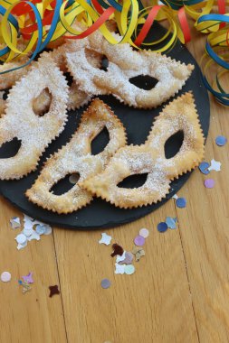 Traditional sweet crisp pastry deep-fried in shape of Carnival mask on a black slate stone plate. Chiacchere or crostoli, bugie, cenci with copy space
