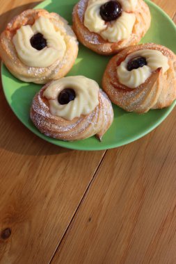 Italian traditional fried Zeppole for St. Joseph (Fathers day). Homemade sweet pastry with custard cream and black cherries on a green plate on wooden table