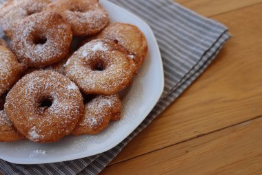 Homemade deep fried apple rings with batter sprinkled with powdered sugar ona white plate on wooden table