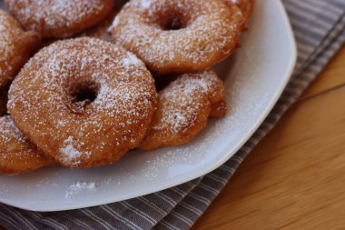 Homemade deep fried apple rings with batter sprinkled with powdered sugar ona white plate on wooden table