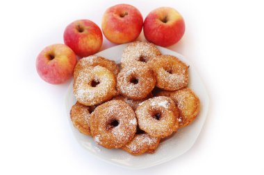 Homemade deep fried apple rings with batter sprinkled with powdered sugar on a plate isolated on white with fresh apples