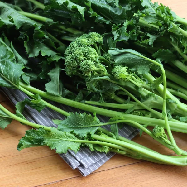 Fresh green turnip plants. Italian cime di rapa with green leaves and blossoms on wooden table. Brassica rapa var. cymosa