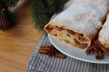Geleneksel elmalı turta, tarçın ve pudra şekeri beyaz bir tabakta, ahşap masada.