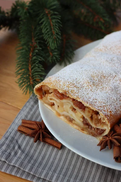 stock image Traditional Apple strudel with cinnamon and powdered sugar on a white plate on wooden table