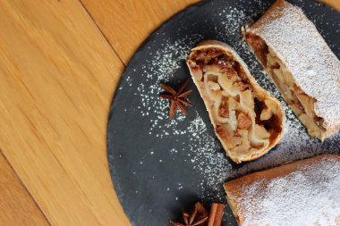 Tarçınlı geleneksel elmalı turta ve pudra şekeri tahta masada siyah bir taş tabakta dilimlenmiş.