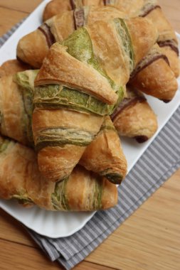 Birçok tatlı çikolata ve pistacchio kruvasan beyaz seramik tepside ahşap masada.