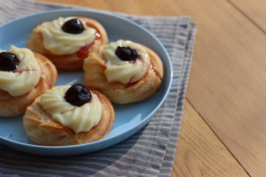 St. Joseph (Babalar Günü) için dört İtalyan usulü kızarmış Zeppole. Dört tatlı pasta kremalı ve ahşap masada mavi bir tabakta siyah kirazlı. 