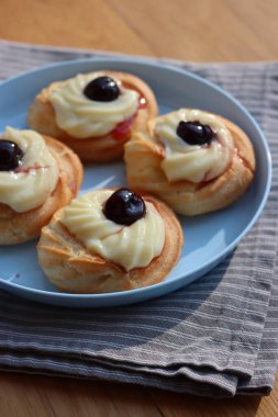 St. Joseph (Babalar Günü) için dört İtalyan usulü kızarmış Zeppole. Dört tatlı pasta kremalı ve ahşap masada mavi bir tabakta siyah kirazlı. 