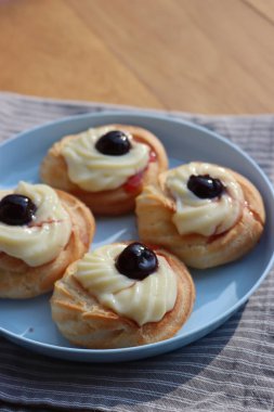 St. Joseph (Babalar Günü) için dört İtalyan usulü kızarmış Zeppole. Dört tatlı pasta kremalı ve ahşap masada mavi bir tabakta siyah kirazlı. 