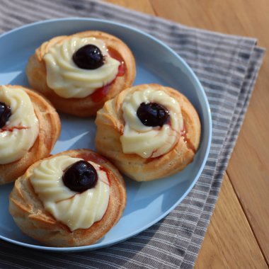 St. Joseph (Babalar Günü) için dört İtalyan usulü kızarmış Zeppole. Dört tatlı pasta kremalı ve ahşap masada mavi bir tabakta siyah kirazlı. 