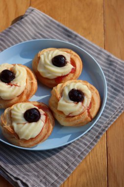 St. Joseph (Babalar Günü) için dört İtalyan usulü kızarmış Zeppole. Dört tatlı pasta kremalı ve ahşap masada mavi bir tabakta siyah kirazlı. 