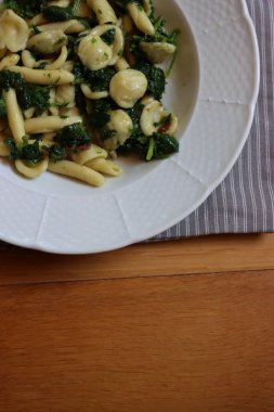 Orecchiette alla pugliese. Geleneksel İtalyan makarnası, şalgam yeşili yapraklı, beyaz bir tabakta, ahşap masada.