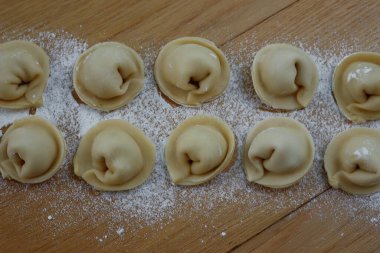 Ev yapımı İtalyan Cappellacci makarnası ve ahşap masa üzerinde beyaz un. Tortellini 'ye benziyor.