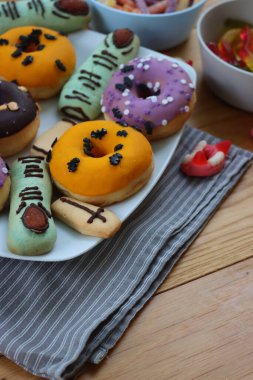 Cadılar Bayramı için çok renkli ve dekore edilmiş çörekler. Üzerinde cadıların parmakları olan kurabiyeler ve ahşap masa üzerinde bir sürü şeker var.