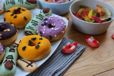 Cadılar Bayramı için çok renkli ve dekore edilmiş çörekler. Üzerinde cadıların parmakları olan kurabiyeler ve ahşap masa üzerinde bir sürü şeker var.