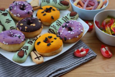 Cadılar Bayramı için çok renkli ve dekore edilmiş çörekler. Üzerinde cadıların parmakları olan kurabiyeler ve ahşap masa üzerinde bir sürü şeker var.