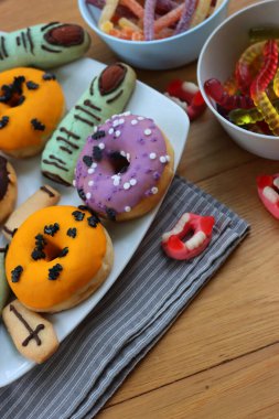 Cadılar Bayramı için çok renkli ve dekore edilmiş çörekler. Üzerinde cadıların parmakları olan kurabiyeler ve ahşap masa üzerinde bir sürü şeker var.