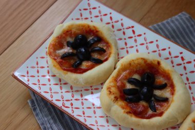  Ahşap masadaki seramik tepside siyah zeytinli Cadılar Bayramı minik örümcek pizzaları.