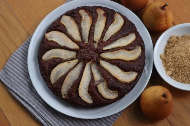 Ev yapımı çikolatalı yuvarlak pasta. Üstünde dilimlenmiş armut var. Tahta bir tabakta.