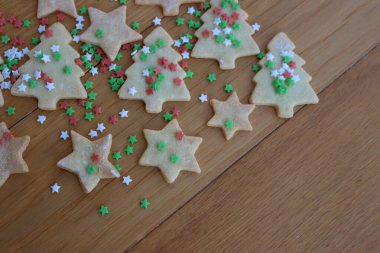 Tahta masanın üzerinde yeşil, kırmızı ve beyaz yıldız şeklinde serpiştirilmiş yıldız ve ağaç şeklinde Noel kurabiyeleri. Seçici odak üzerine Noel şenliği arka planı