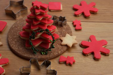 Kırmızı şeker kaplı yıldız şeklindeki kurabiyelerden yapılmış Noel ağacı ve beyaz arka planda yeşil bir çelenk.